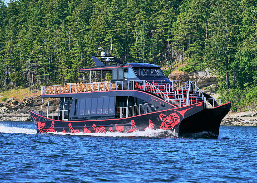 Salish Sea Tours boat cruising on Elliott Bay with forested shoreline behind